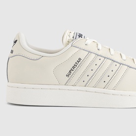Adidas Superstar trainers in off-white leather with tonal three stripes, navy branding, and white rubber shell toe sole