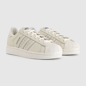 Adidas Superstar trainers in off-white with tonal three stripes, shell toe, and carbon accent detailing on a cream sole