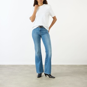 Model wearing Seven Jeans The Leggy Bootcut Jeans in Coastline mid-wash denim, mid-rise bootcut silhouette, styled with white T-shirt and black