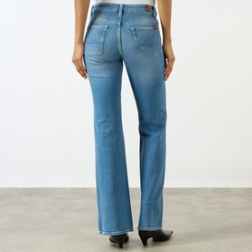 Model wearing Seven Jeans The Leggy Bootcut Jeans in Coastline, mid-rise, mid-wash blue bootcut denim, shown from behind with black heels.