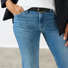 Model wearing Seven Jeans The Leggy Bootcut Jeans in Coastline mid-wash denim, styled with a black belt and blazer.