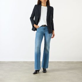 Model wearing Seven Jeans The Leggy Bootcut Jeans in Coastline mid-wash denim, styled with a black blazer, white tee and black heeled boots.