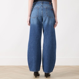 Model wearing Seven Jeans wide-leg jeans in Skyfrost blue denim, shown from behind, with curved barrel-leg silhouette and high waist