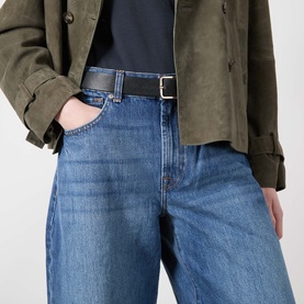 Model wearing Seven Jeans Skyfrost wide-leg denim jeans in light blue wash, styled with an olive jacket and black belt.