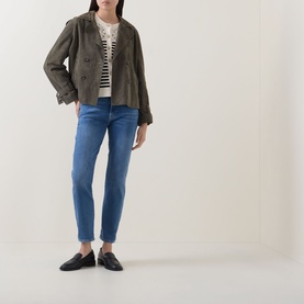 Model wearing Seven Jeans Coastline skinny jeans in mid-blue, styled with a khaki jacket, striped top and black loafers.
