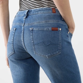 Model wearing Seven Jeans Slim jeans in Coastline blue denim, rear view showing back pockets and signature logo detail.