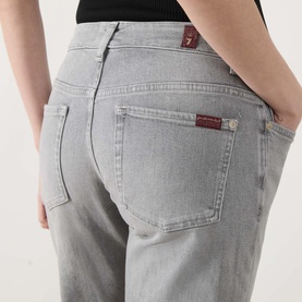 Model wearing light grey slim-fit jeans with burgundy branded back pocket tab, close-up rear view, styled with black top.