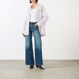 Model wearing Seven Jeans Lotta Wide-Leg Jeans in Blue Core mid-wash denim, styled with a pale lilac oversized shirt and black heeled boots.