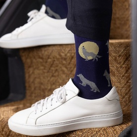 Model wearing Swole Panda dark blue socks with wolf and moon print, styled with white leather trainers and navy trousers.