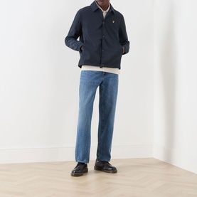 Model wearing Lyle & Scott Eagle Logo Coach Jacket in Dark Navy with light blue jeans and black leather shoes.