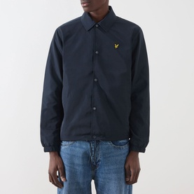 Model wearing Lyle & Scott Eagle Logo Coach Jacket in Dark Navy with snap buttons and yellow logo, styled with light blue jeans.