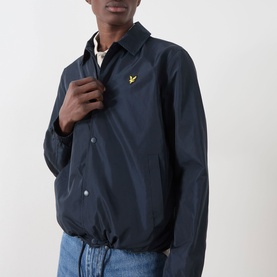 Model wearing Lyle & Scott Eagle Logo Coach Jacket in Dark Navy with snap buttons and gold eagle logo, styled with light blue jeans.