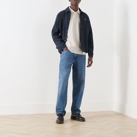 Model wearing Lyle & Scott Eagle Logo Coach Jacket in Dark Navy with cream polo, blue jeans and black loafers.