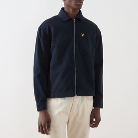 Model wearing Lyle & Scott Eagle Logo Overshirt in Dark Navy with zip fastening and gold eagle logo, styled with cream trousers.