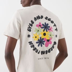 Model wearing Lyle & Scott Logo Nature Graphic T-Shirt in Putty, rear view showing circular floral graphic print with brand lettering.