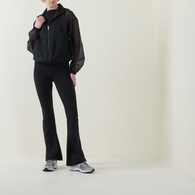 Model wearing Spanx jacket in Very Black with sheer sleeves, styled with matching black flared leggings and grey trainers
