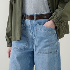 Model wearing Spanx SPANXsupersmooth&trade; Authentic 360 Lightweight Utility Barrel Leg Jeans in Seaside Blue with olive utility jacket and brown belt.