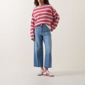 Model wearing red and white striped knit sweater with wide-leg cropped blue jeans and white trainers with red stripes