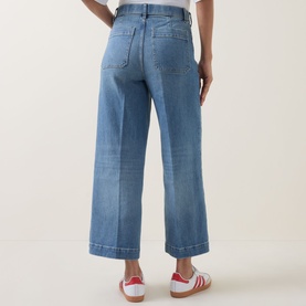 Model wearing light blue wide-leg cropped jeans, rear view, styled with white and red trainers
