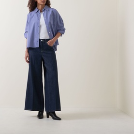Model wearing Spanx SPANXsupersmooth&reg; Authentic 360 Lightweight Wide-Leg Jeans in Deep Sea, styled with a blue shirt and black heeled boots.