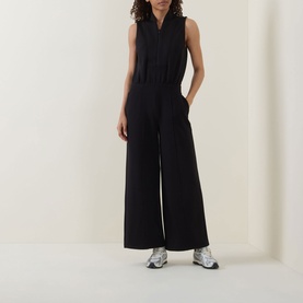 Model wearing Spanx AirEssentials&reg; Half-Zip Jumpsuit in Very Black, sleeveless with shawl collar and wide-leg fit, styled with silver trainers.