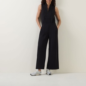 Model wearing Spanx AirEssentials&reg; Half-Zip Jumpsuit in Very Black, sleeveless wide-leg style with shawl collar, styled with white trainers.