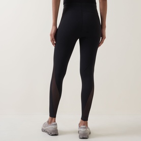 Model wearing black high-waist leggings with sheer mesh panel inserts at lower leg, styled with grey trainers, rear view