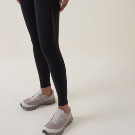 Model wearing black leggings styled with light grey chunky-soled trainers, cropped below the waist to show legs and feet only.