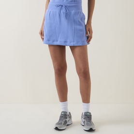 Model wearing Spanx BoostUp Skort 15" in Hyacinth, mini length with drawstring waist and side pockets, styled with white socks and grey trainers.