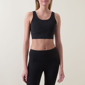 Model wearing Spanx Sheer Panel Sports Bra in Very Black with scoop neckline and wide underband, styled with matching black leggings.