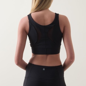 Model wearing Spanx Sheer Panel Sports Bra in Very Black, back view showing scoop neckline, sheer mesh panels and wide underband, styled with black
