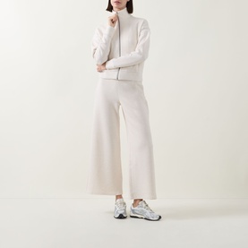 Model wearing Spanx AirEssentials Wide Leg Track Pants Petite in Oatmeal Heather, styled with matching zip-up top and white trainers.
