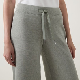 Model wearing Spanx AirEssentials Wide Leg Track Pants Petite in Sage Heather, showing elasticated drawstring waist and wide-cut leg detail.