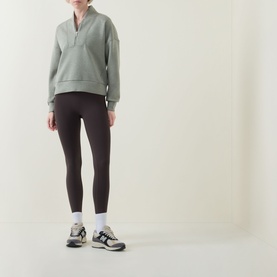 Model wearing Spanx AirEssentials&reg; Half-Zip Sweatshirt in Sage Heather with dark leggings and grey trainers.