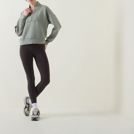 Model wearing Spanx AirEssentials&reg; Half-Zip Sweatshirt in Sage Heather with shawl collar, styled with dark leggings and trainers.