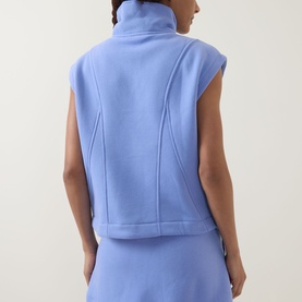 Model wearing Spanx BoostUp Half-Zip Sweatshirt in Hyacinth, showing back view with cap sleeves, funnel neck and seam detailing.