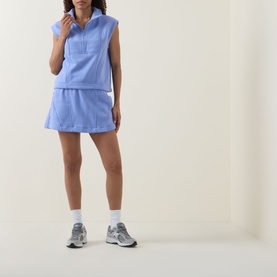 Model wearing Spanx BoostUp Half-Zip Sweatshirt in Hyacinth with matching mini skirt, white socks and grey trainers.