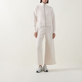Model wearing Spanx AirEssentials&reg; Track Jacket in Oatmeal Heather with zip fastening, styled with matching wide-leg trousers and trainers.