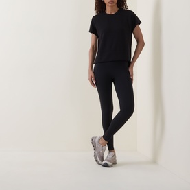 Model wearing Spanx AirEssentials T-Shirt in Very Black with matching black leggings and grey trainers.