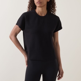 Model wearing Spanx AirEssentials T-Shirt in Very Black, crew neck, short sleeves, slightly cropped length, paired with black leggings.