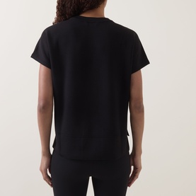 Model wearing Spanx AirEssentials T-Shirt in Very Black, rear view showing crew neckline, short sleeves, and slightly cropped straight hem.