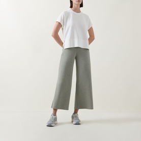 Model wearing Spanx AirEssentials T-Shirt in Powder with wide-leg cropped trousers and grey trainers.