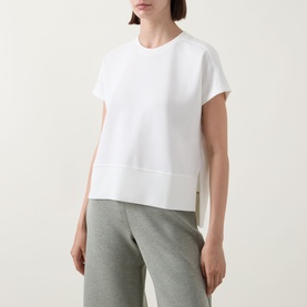 Model wearing Spanx AirEssentials&reg; T-Shirt in Powder with round neck, short sleeves and split side seams, styled with grey joggers.