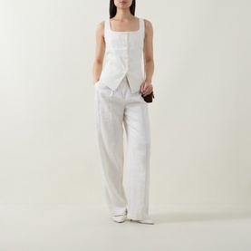 Model wearing Spanx ivory sleeveless square-neck top with asymmetric hem, styled with wide-leg white trousers and white heels