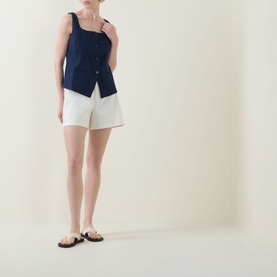Model wearing Spanx Timeless Navy sleeveless button-front top with white shorts and black flat sandals