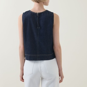 Model wearing Spanx Lightweight Denim Shell Tank in Deep Sea, back view showing zip fastening and contrast topstitch, styled with white trousers.