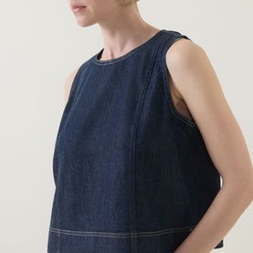 Model wearing Spanx Lightweight Denim Shell Tank in Deep Sea, sleeveless with round neckline and contrast topstitch details visible.