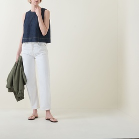 Model wearing Spanx Lightweight Denim Shell Tank in Deep Sea with white straight-leg jeans, carrying a khaki jacket, styled with tan flat sandals.
