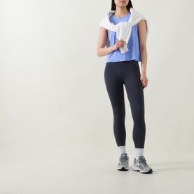 Model wearing Spanx Hyacinth active top, styled with dark navy leggings, white draped towel, and grey trainers