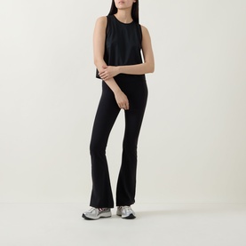 Model wearing Spanx Sheeriours Panel Performance Top in Very Black, sleeveless with round neck, styled with black flared trousers and grey trainers.